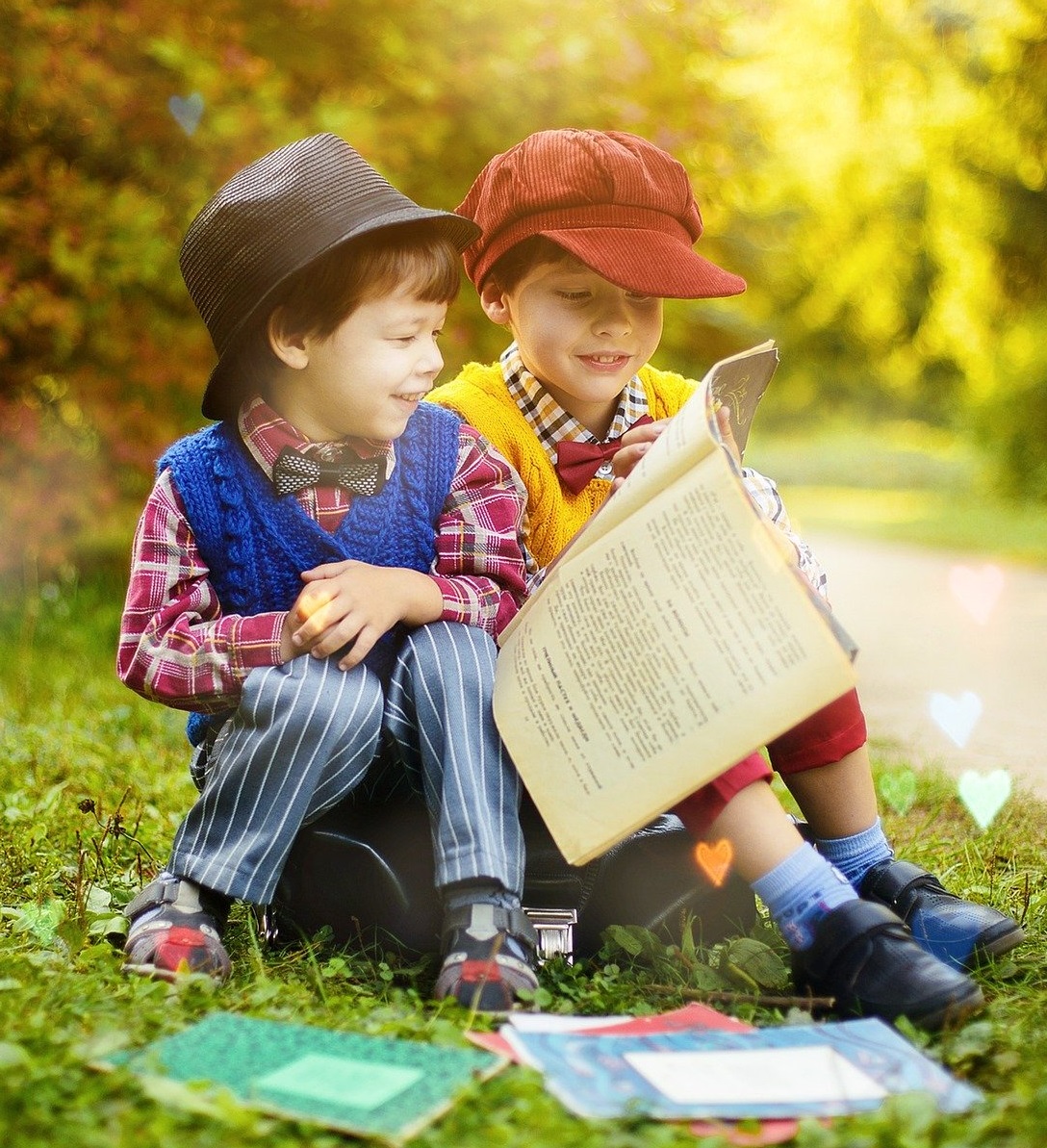 two childern sitting on the grass next to a path reading a shared book. bright sunlight behind them