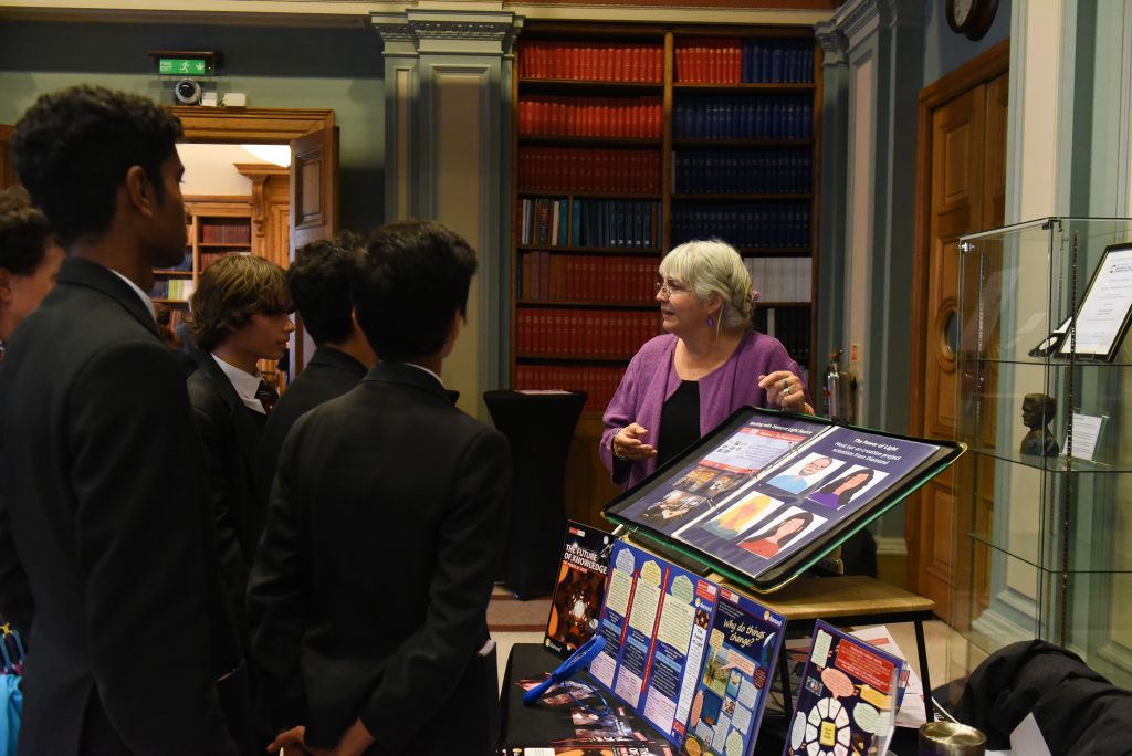 This image is from exhbition at the Future of Knowledge conference at the Royal Society of Chemistry A research fellow is sharing key parts of a exhibit on the Power of Light project with a group of students from a school in London.